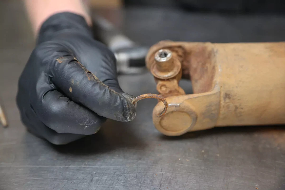 A mechanic wearing a black glove holds the inside clip of a driveshaft after removing it.