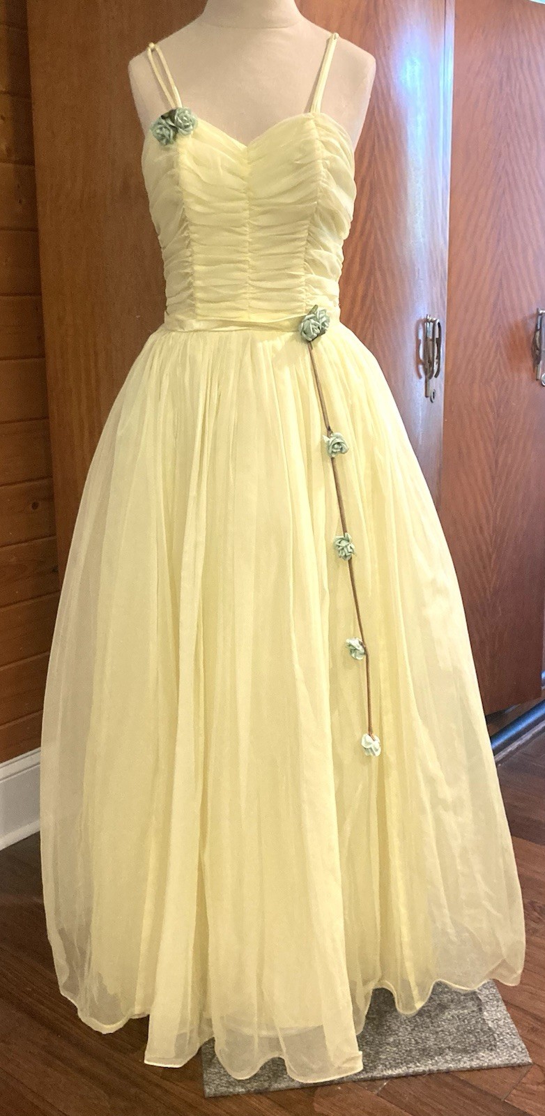 Pale yellow chiffon gown with rosette trim down the skirt.
