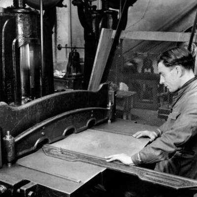 Worker works machine which cuts into squares metal sheet which wil- Old Photo