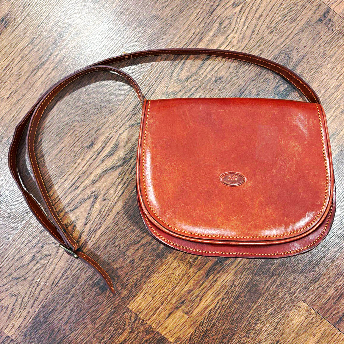 Cognac brown leather saddle bag with a rounded flap and adjustable strap.