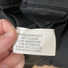 White fabric tag on inner collar of black solid three-button blazer, with black text reading “Professionally Dry Clean Low Moisture Made in U.S.A.”