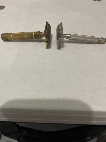 Two vintage Gillette safety razors, one brass and one silver, with flat rectangular handles and visible branding.