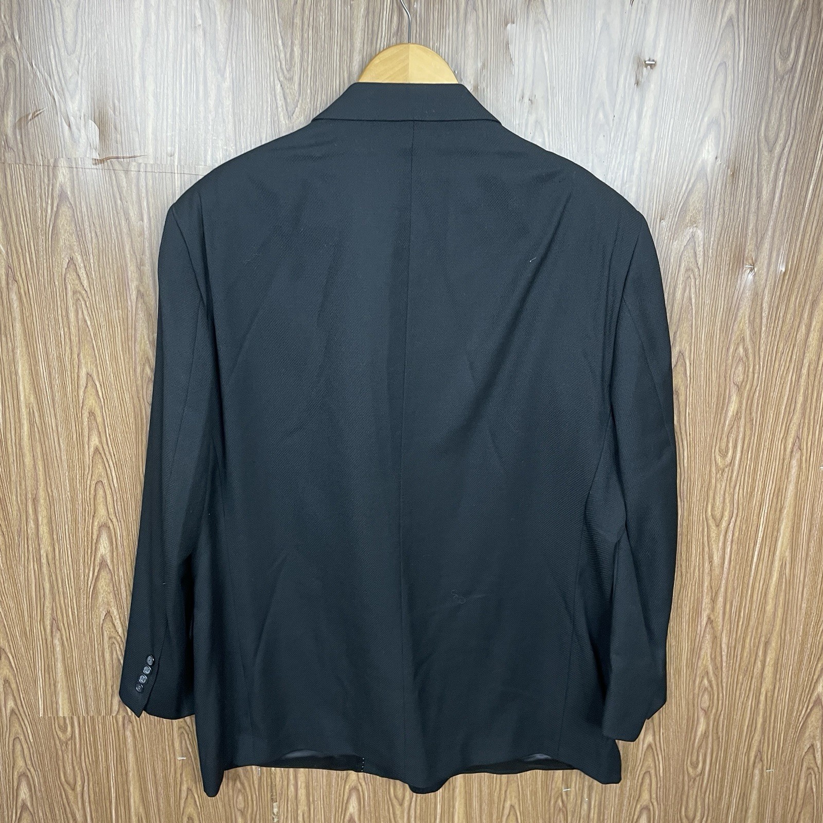 Black men's blazer jacket with notch lapels, three-button front closure, and long sleeves, hanging on wooden hanger.