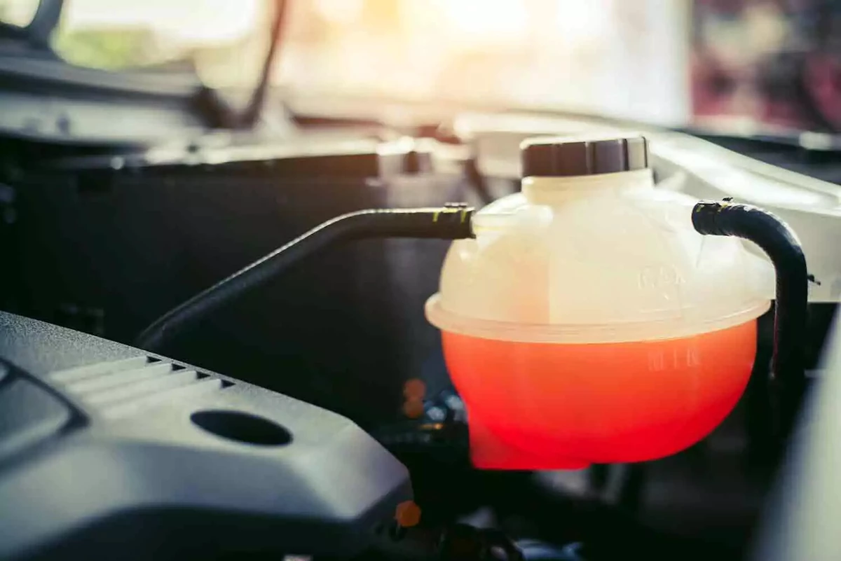 An engine coolant overflow tank, filled with orange coolant.