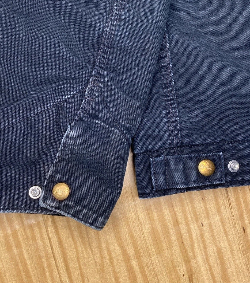 Black Carhartt J01 BLK Detroit jacket with front snap buttons, two chest flap pockets, and white stitching on collar and seams.