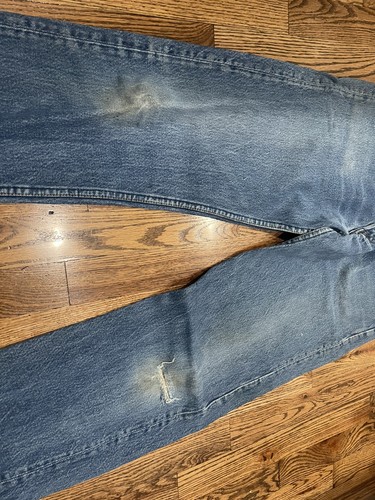 Vintage Levi’s 501XX blue made in USA 80s jeans with frayed front seam and small white tear repair patch on right thigh.