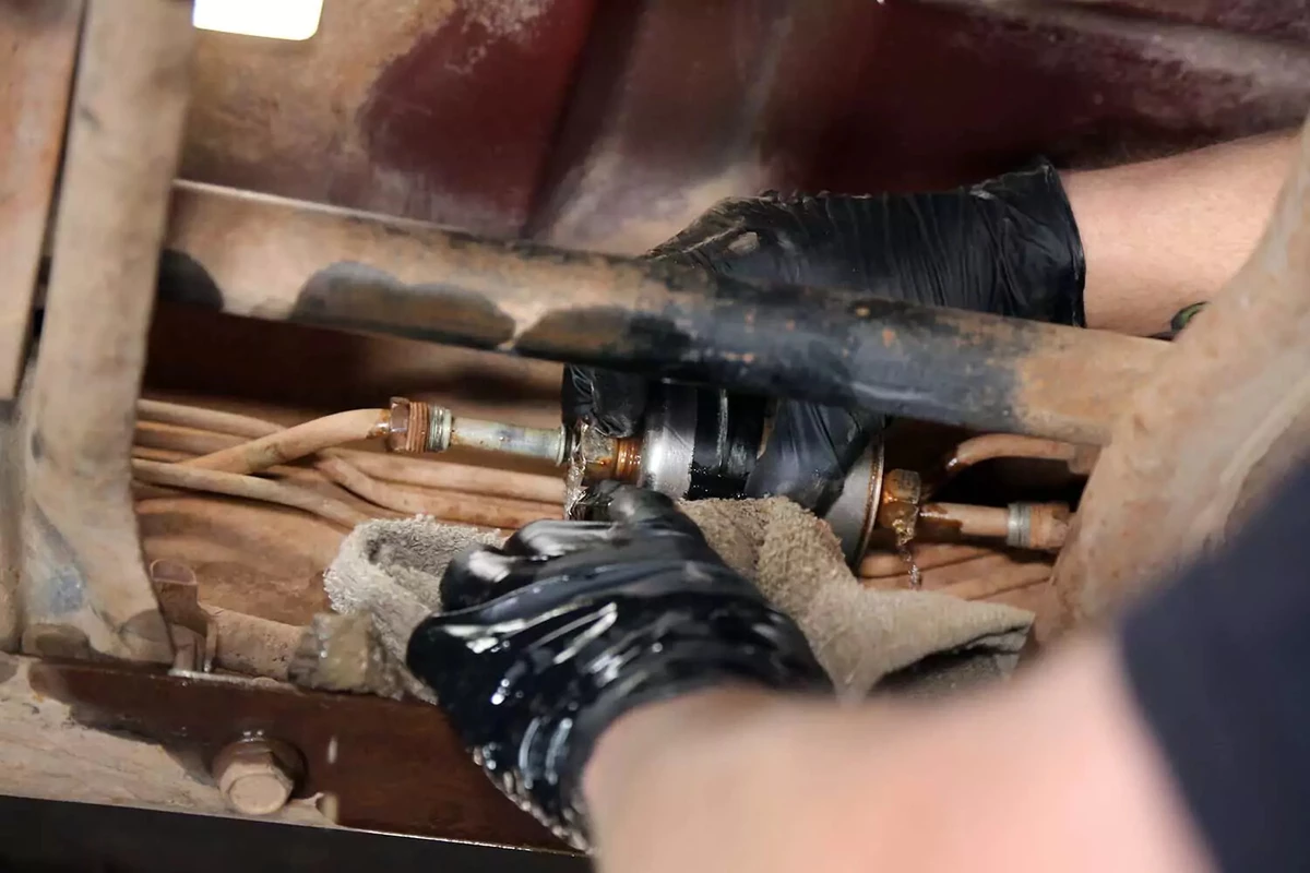 A mechanic holds a towel to catch spilled fuel while separating the filter from the fuel tank line.