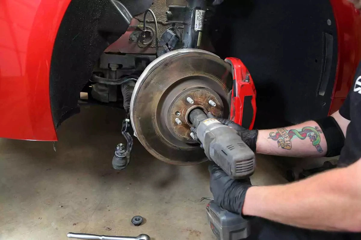 A mechanic uses an impact gun with an axle socket to remove the axle nut.