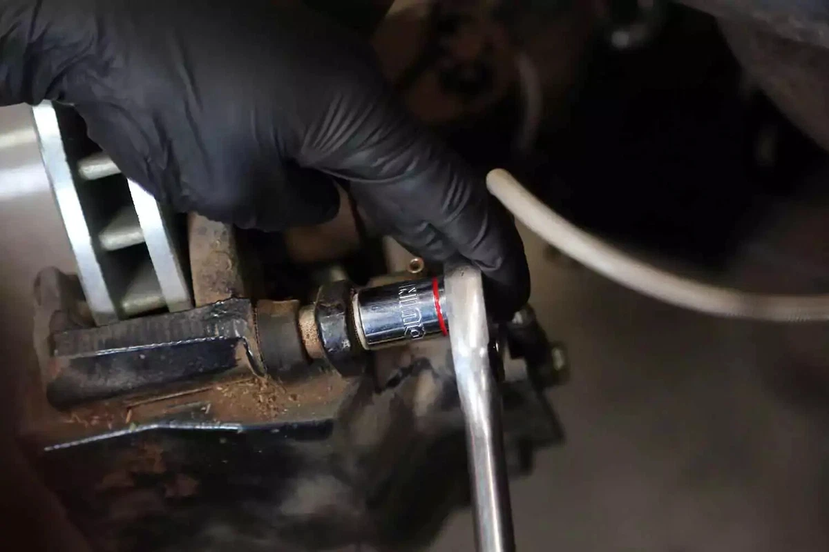 A mechanic removing a bolt from a brake caliper with a ratchet wrench.