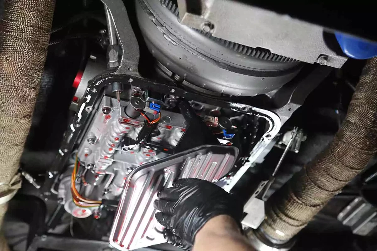 A mechanic wearing a black glove removes the transmission filter.