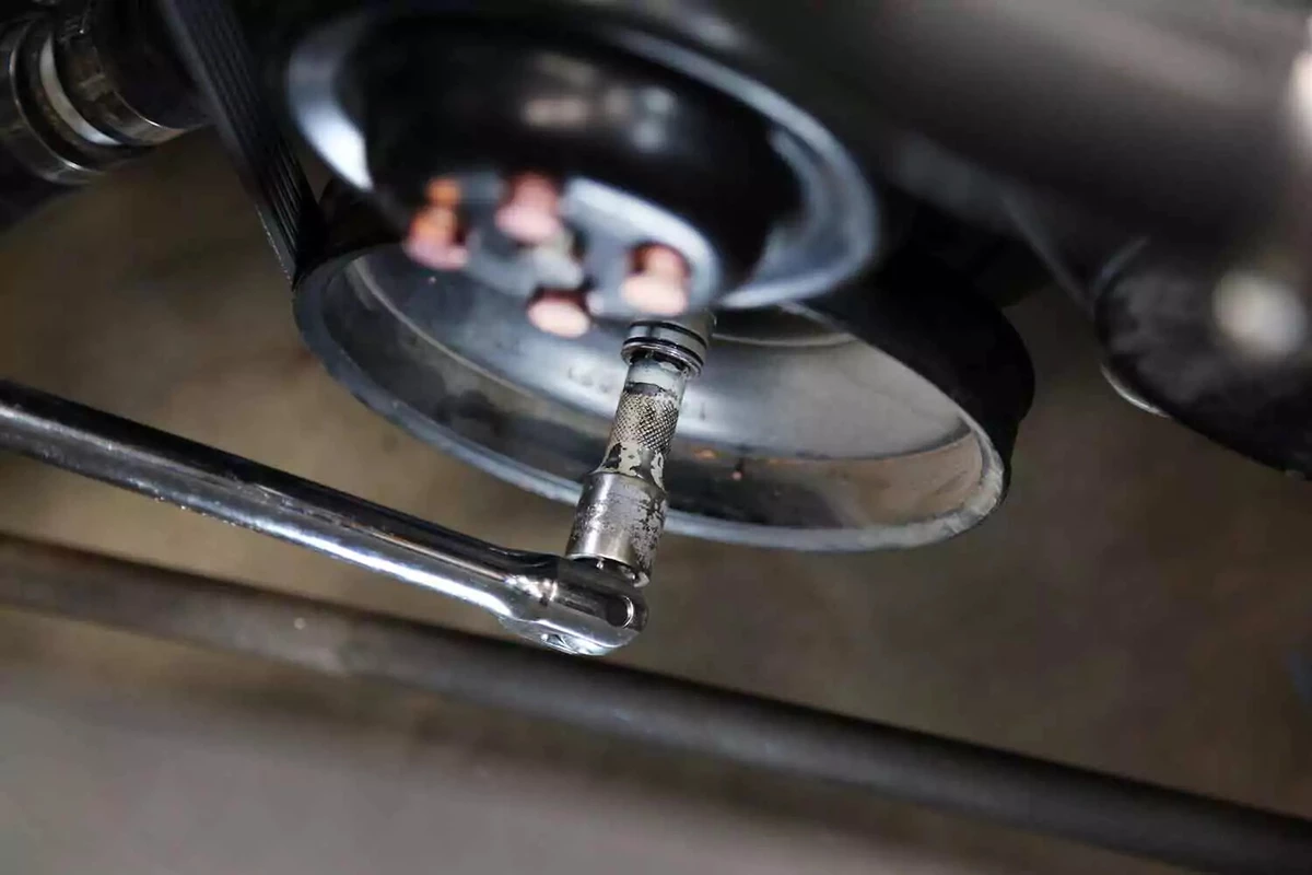 A mechanic uses a breaker bar with a socket to spin the crank bolt to TDC.