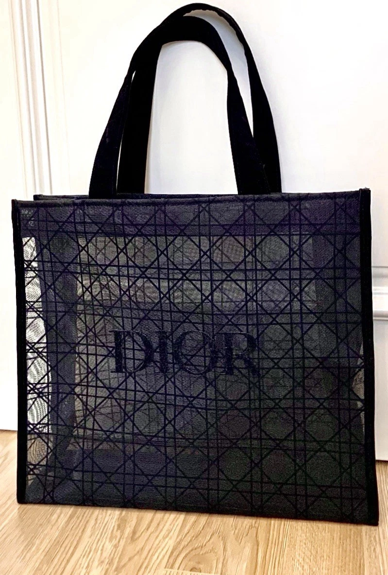 Black lace mesh tote with geometric pattern and �DIOR� logo, black handles, on wooden surface.