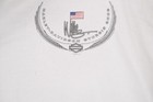 White vintage Harley-Davidson Sturgis 2002 polo shirt with black embroidered winged logo and red, white, and blue USA flag.