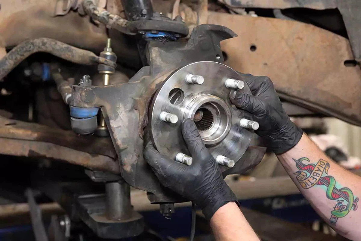A mechanic slides the new wheel bearing hub into the knuckle.