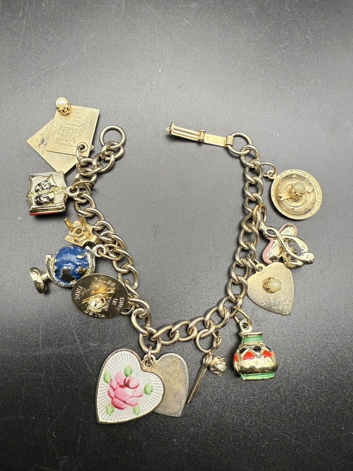 Gold-tone charm bracelet loaded with heart, globe, diary, and enamel charms