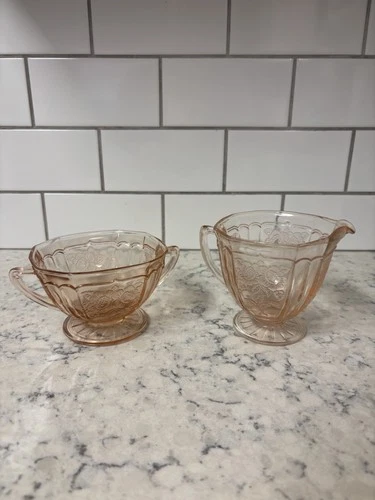 Pink Depression glass creamer and sugar set with floral pattern.