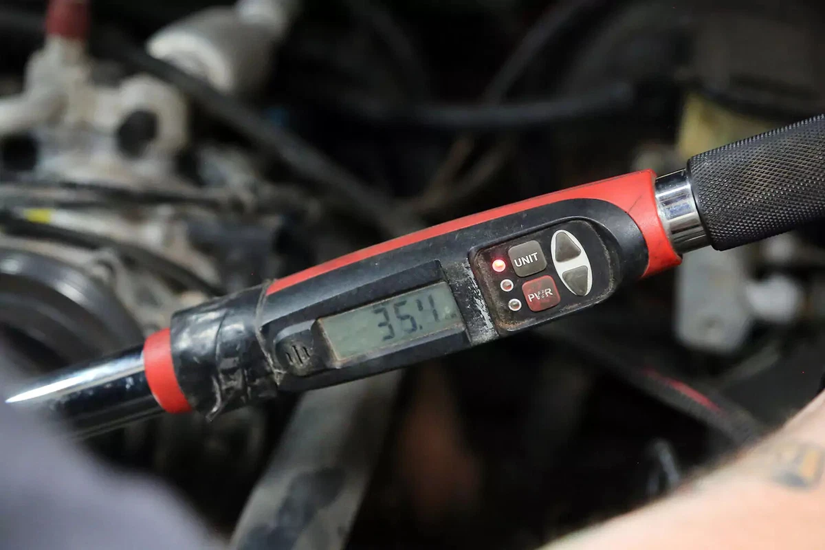 A mechanic tightens the idler pulley bolt with a torque wrench to specifications.