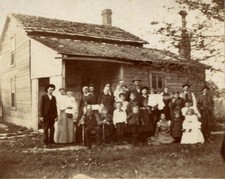 LARGE FAMILY POSED IN FRONT OF RURAL HOMESTEAD. SILVER PRINT.