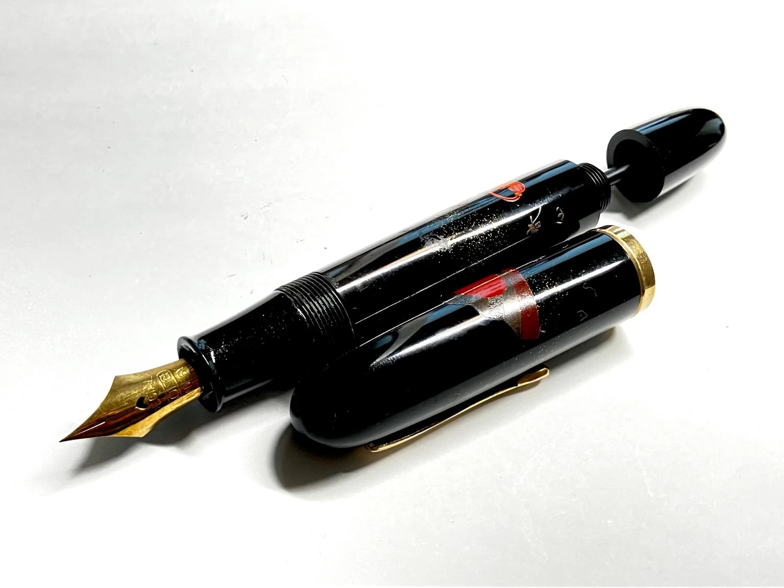 Black vintage fountain pen with gold nib, red-urushi body, and ornate Kabuto-style tip on white background.