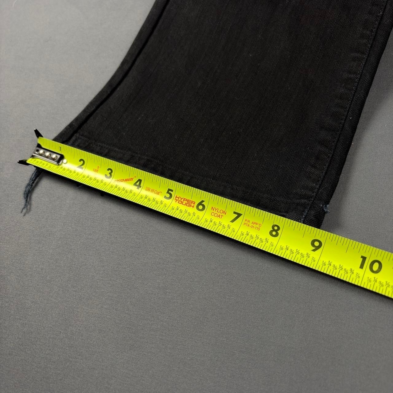 Black faded bootcut jeans with frayed hems, yellow measuring tape along the waistband, showing size 8.