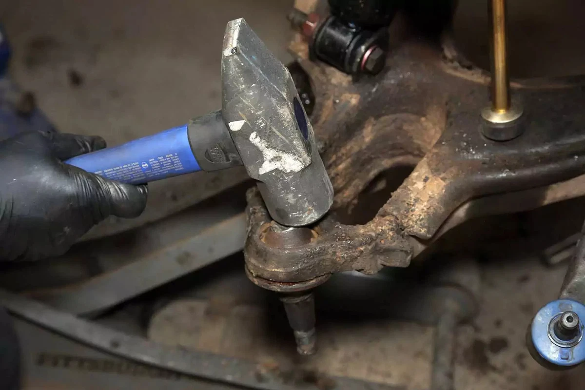 A mechanic uses a five-pound hammer to drive the ball joint out of the arm.