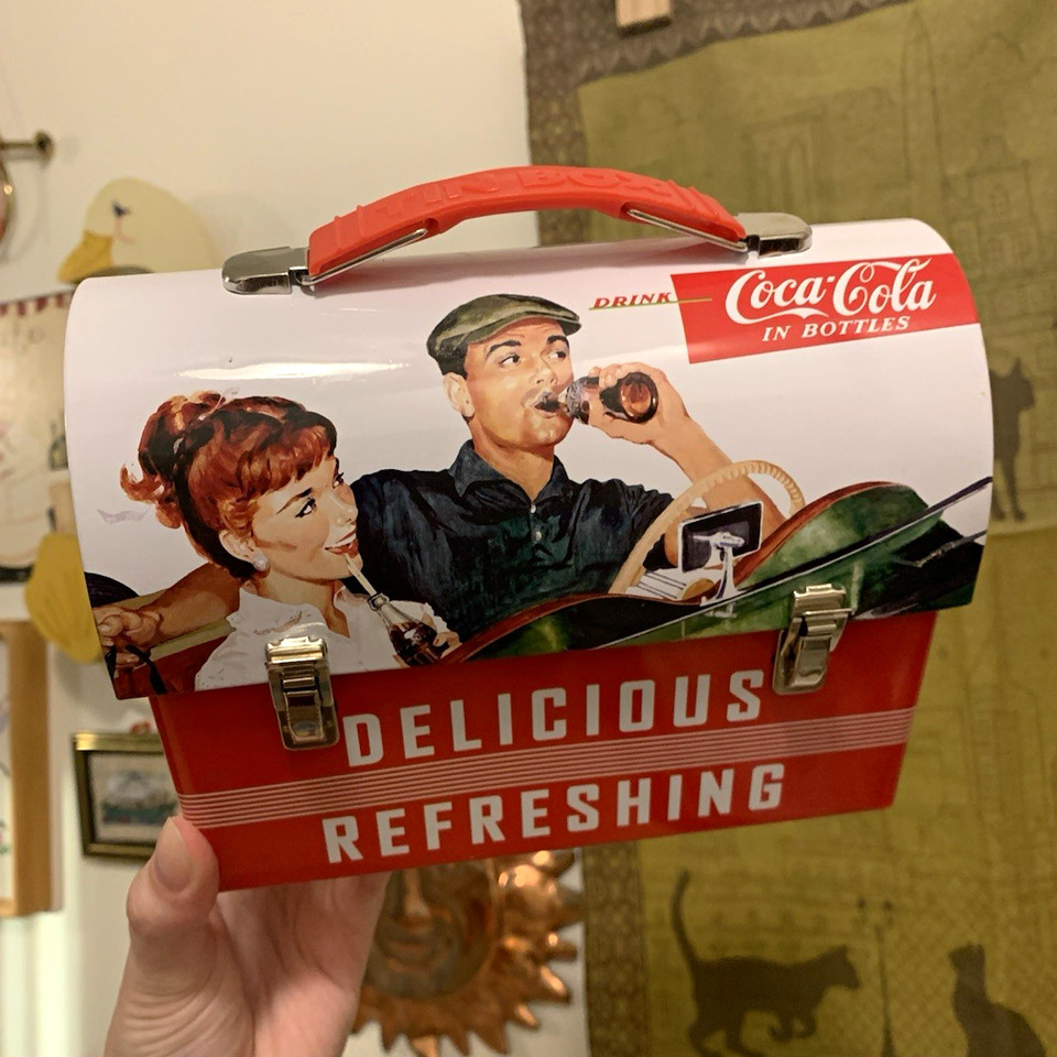 A charming Coca-Cola mini tin lunch box featuring a 1950s scene — the kind of branded nostalgia piece that looks great on a shelf.