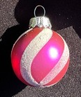 Round glass holiday ball with pink/silver striped and solid red designs, silver cap, on black background.