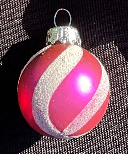 Round glass holiday ball with pink/silver striped and solid red designs, silver cap, on black background.
