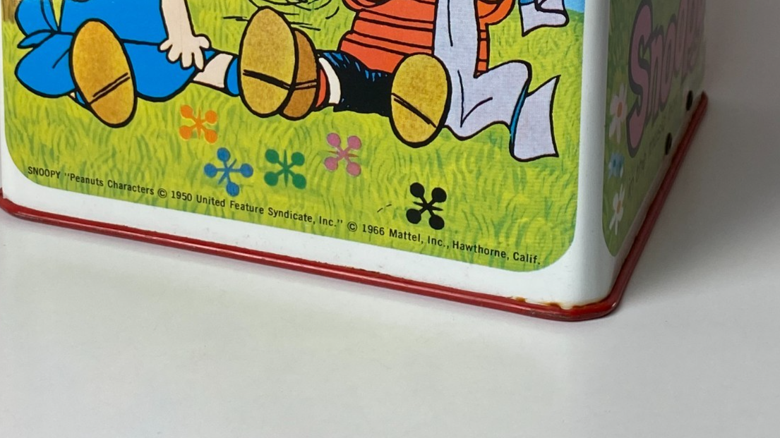 Snoopy in a red box with Woodstock, green grass, orange flowers, and text “Made in U.S.A.”