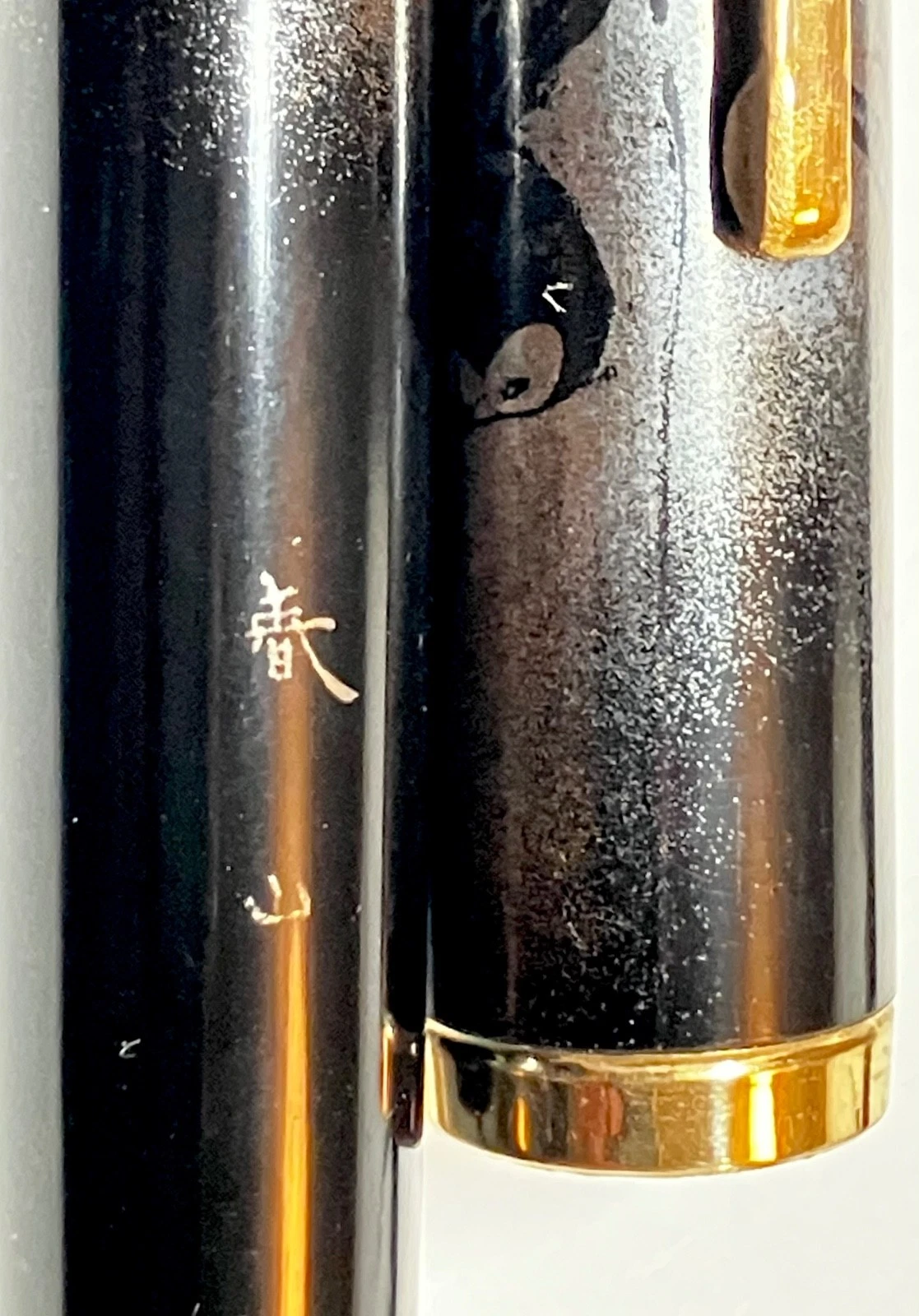 Black vintage fountain pen with gold band, urushi maki-e brushstroke, and gold ink details on textured barrel.