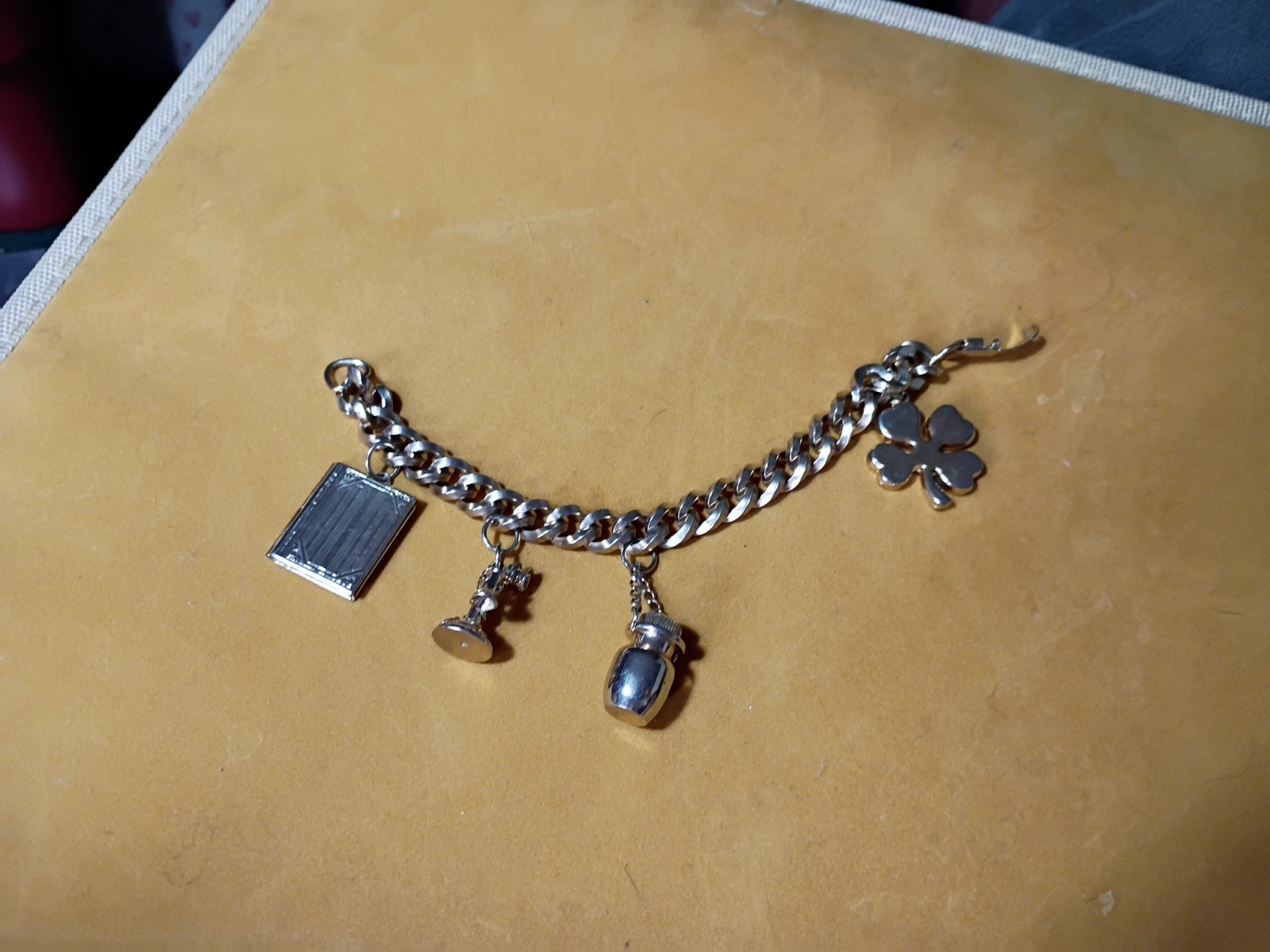 Gold-tone charm bracelet with a book charm, an egg-shaped charm, and a four-leaf clover charm