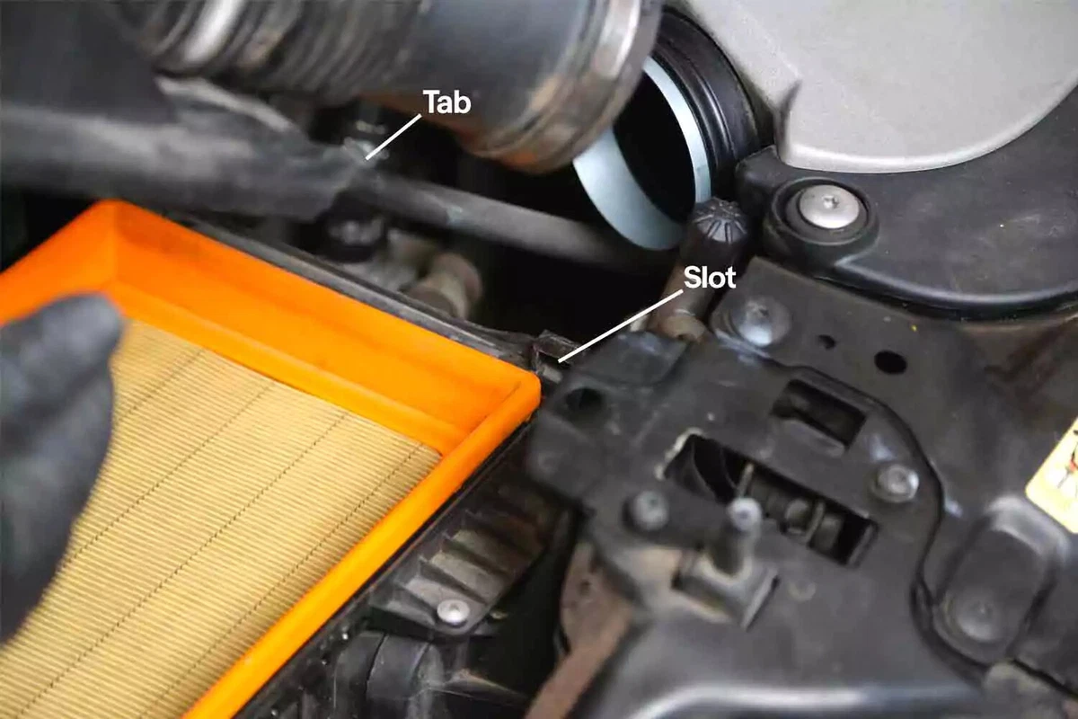 A new air filter shown with callouts pointing to the tab on the filter and the slot in the filter air box.