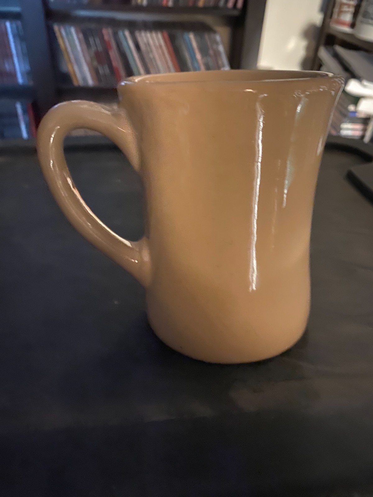 Beige ceramic mug with a curved handle, white logo, and “Made in U.S.A.” text on a dark surface.