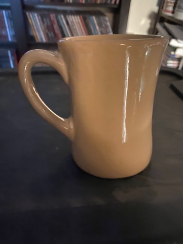Beige ceramic mug with a curved handle, white logo, and “Made in U.S.A.” text on a dark surface.