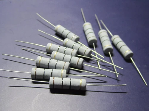 High power 5W metal oxide film resistors with gold leads, arranged in rows on a dark blue surface.