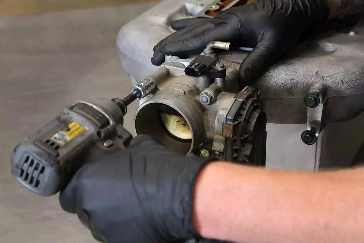 A mechanic reinstalls the throttle body using an impact driver.