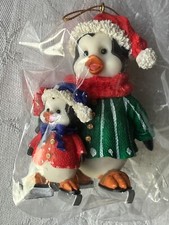2 PENGUINS TOGETHER ON ICESKATES WEARING HOLIDAY CLOTHING CHRISTMAS ORNAMENT.