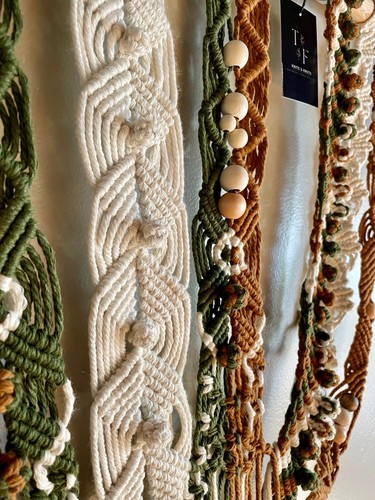 Large white macrame wall hanging with intricate braided patterns and wooden beads, displayed among similar pieces.