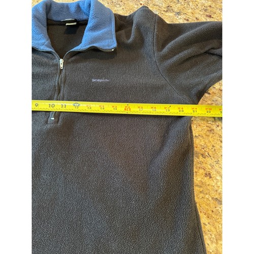 Black quarter zip fleece pullover with light blue collar, laid flat on surface with measuring tape.