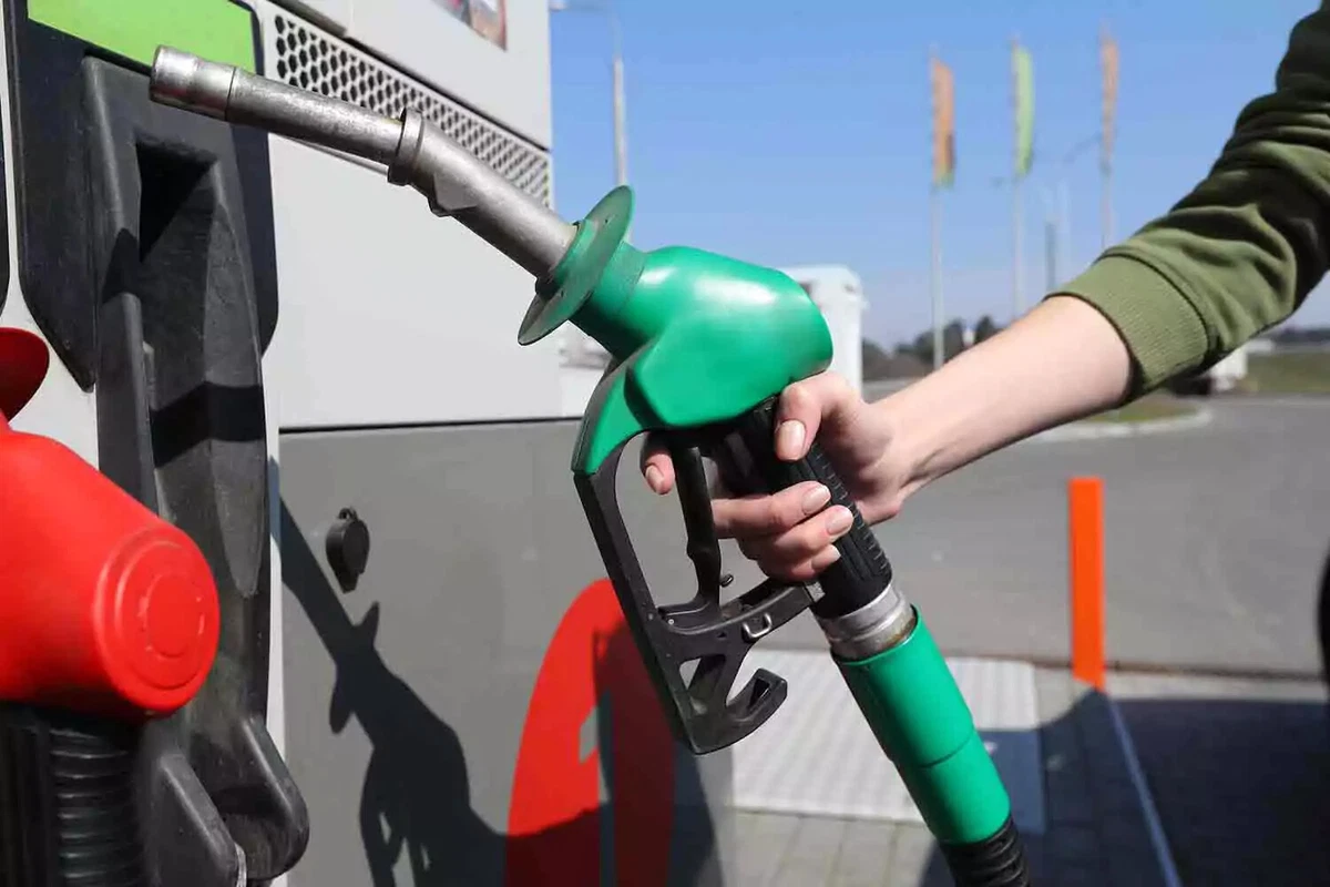 A driver removes a green nozzle from a service station pump.