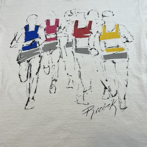White T shirt with black line art of runners in blue, red, yellow, and gray, signed “Reebok” in black ink.