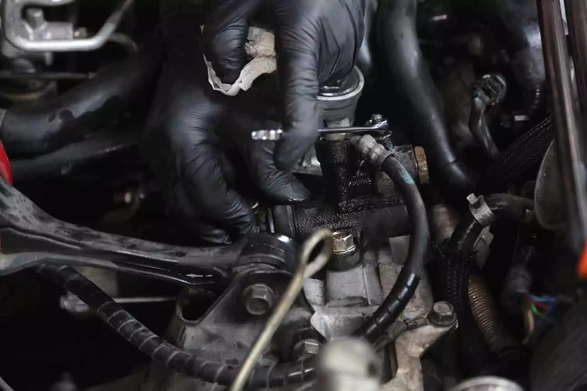 A mechanic wearing black gloves performs a final bleed on a slave cylinder.