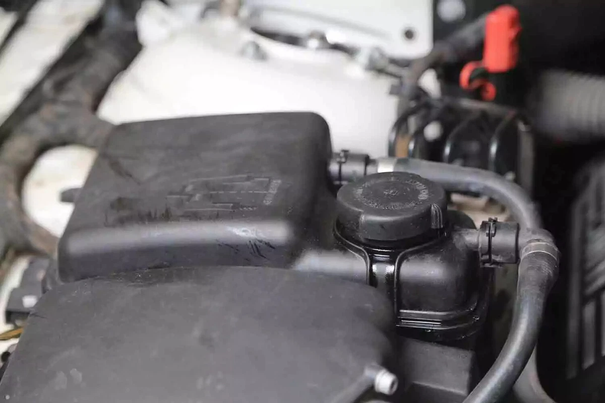 The black fill cap attached to the black expansion coolant tank of a vehicle.