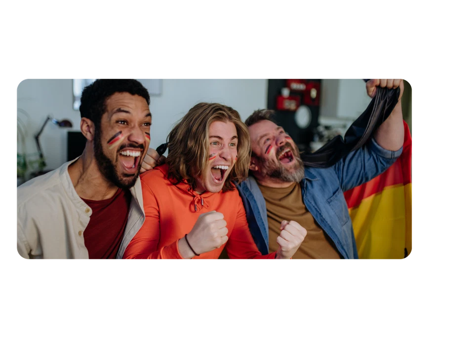 Drei junge Männer jubeln euphorisch. Sie haben die Deutschlandfahne auf die Wangen geschminkt, einer hält sie auch als Umhang