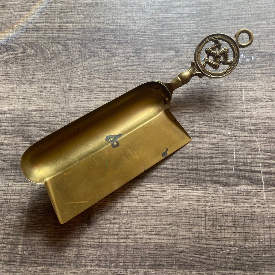 A solid brass Victorian-era crumb scoop and silent butler featuring the three-legged Triskelion of the Isle of Man — utterly obscure, impeccably weird, and genuinely useful on a formal table.