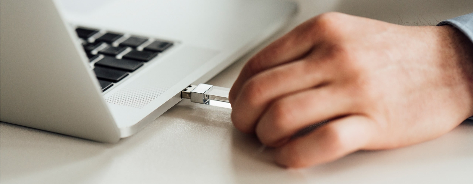 Nahaufnahme von einer Person, die einen transparenten USB-Stick in einen Laptop steckt