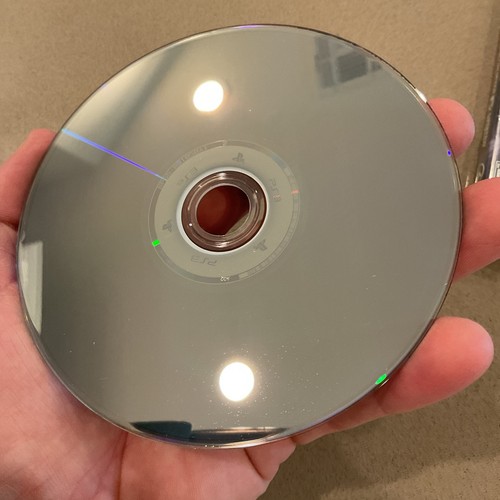 Silver PS3 game disc with black center hole, gold ring, and white label showing Need for Speed Most Wanted Hot Pursuit Rivals Run.