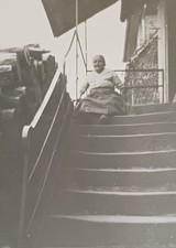 Alte Frau sitzt ganz oben auf einer langen Treppe vorm Haus Foto