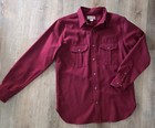 Red Filson virgin wool guide shirt with long sleeves, two chest flap pockets, and button-down collar on wooden floor.