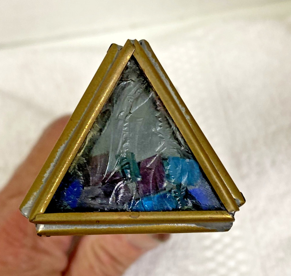 A brass and stained-glass triangular prism kaleidoscope — the kind of desktop object that stops visitors mid-sentence.
